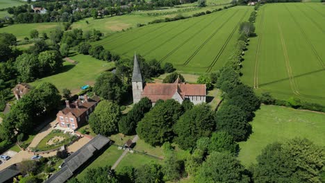 An-aerial-push-out-shot-of-St-John-the-Evangelist-church-in-Ickham,-Kent,-with-parts-of-the-village-visible-as-the-camera-zooms-out