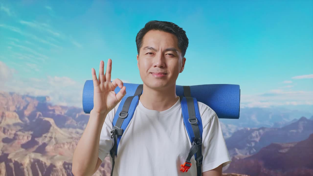 Close Up Of Asian Male Hiker With Mountaineering Backpack Smiling And Showing Okay Gesture To Camera While Traveling At The Top Of Mountain