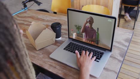 mujer tomando un bocadillo mientras hace una videollamada en una computadora portátil en una cafetería