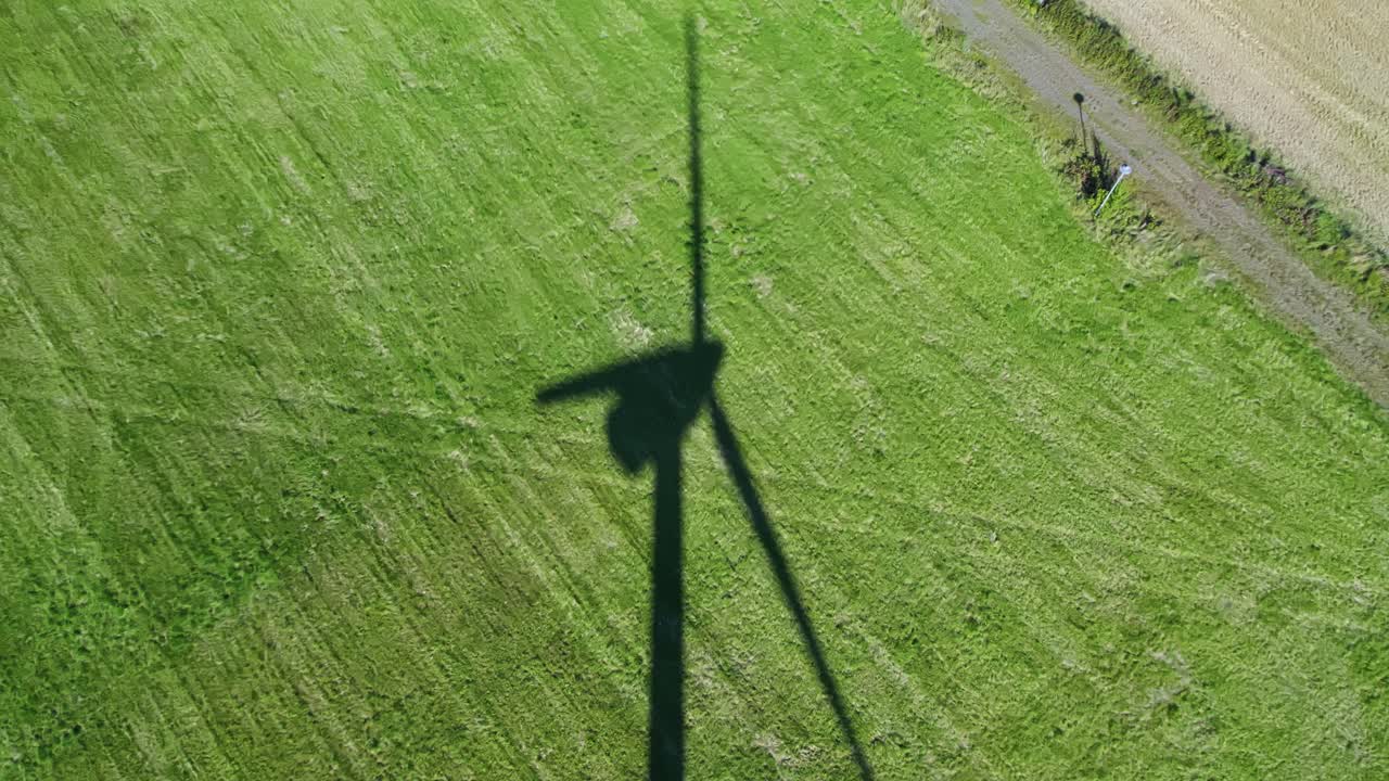 Shadow of wind turbine on green field, aerial view symbolizing clean energy focus