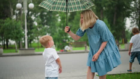 a mother holds an umbrella, playfully talking with her young son as he reaches out to touch the umbrella