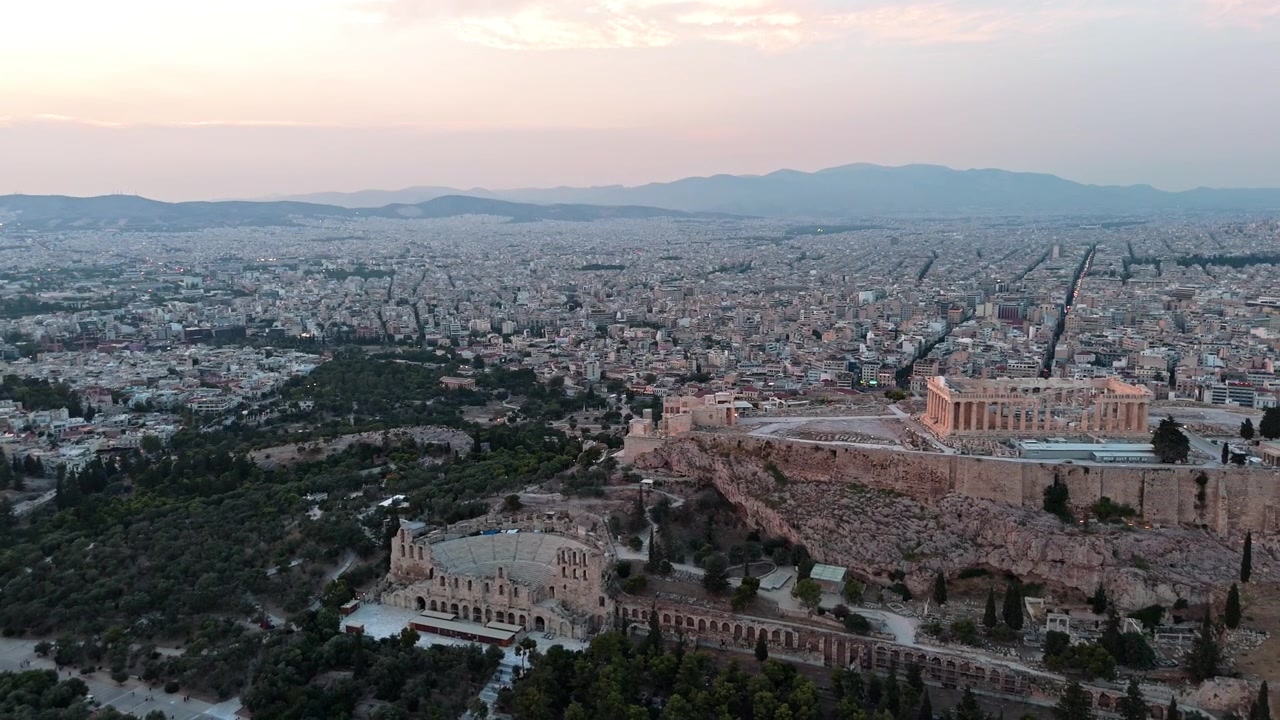 L'antica Acropoli di Atene con il Partenone e l'Odeon di Erode Attico si erge su parchi e griglia urbana nella morbida luce del tramonto
