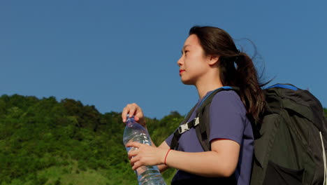 slow motion portrait of female solo young asiatic backpacker drinking water after long day of hiking trekking in mountains destination