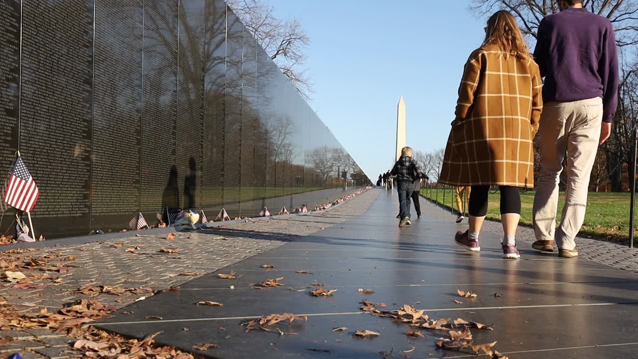 아이들과 함께 가족이 워싱턴 dc의 베트남 전쟁 기념 벽을 지나가고, 배경에는 워싱턴 기념비가 있습니다.