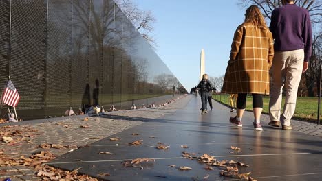 family with children walk past the vietnam war memorial wall in washington, dc with the washington monument in the background