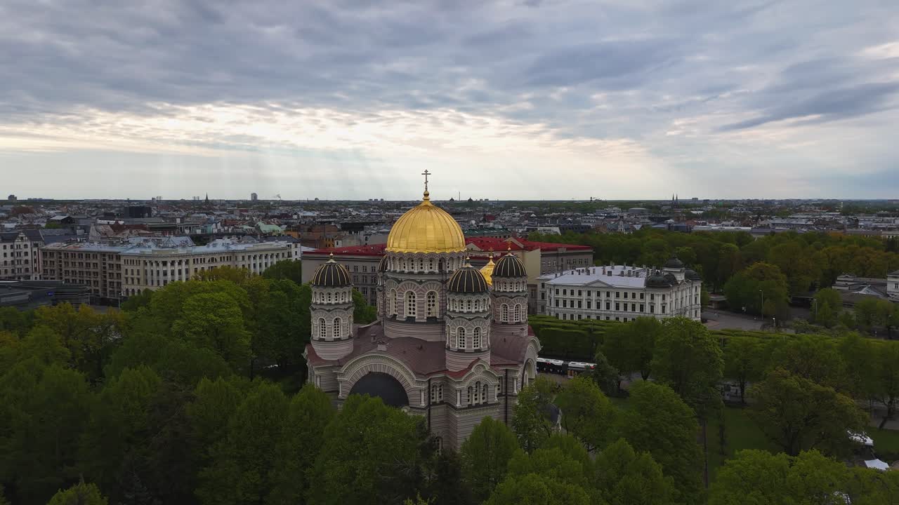 Neo-Byzantine Orthodox cathedral in Riga stands bright among lush green trees.