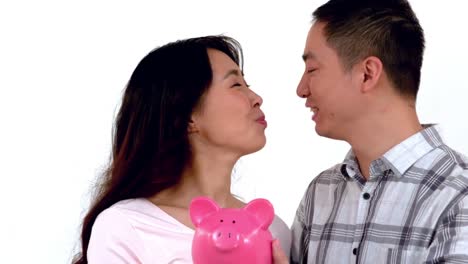 asian couple holding a piggy bank while kissing themselves