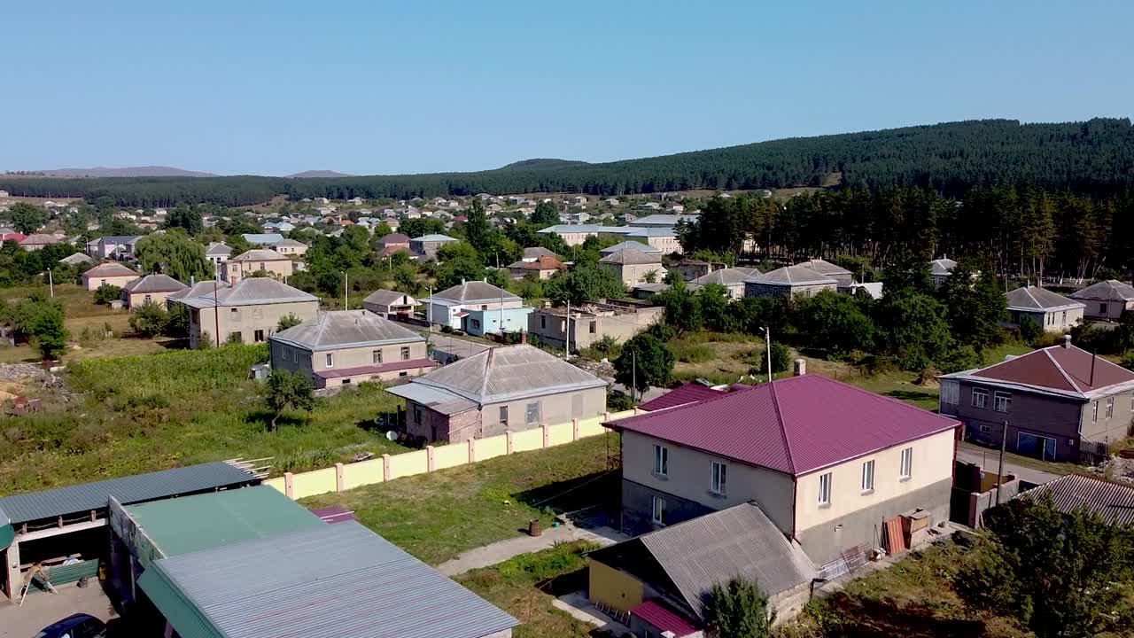 Enjoy the peaceful view of a charming village surrounded by greenery and mountains. This location features traditional houses under a clear blue sky