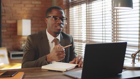 Hombre-De-Negocios-Negro-Hablando-En-Una-Llamada-Web-En-Una-Computadora-Portátil-Y-Tomando-Notas