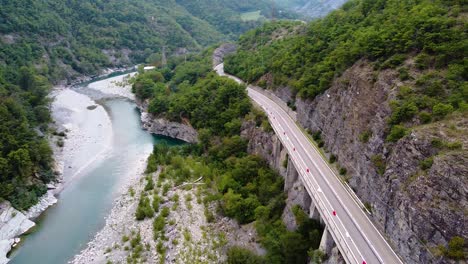 Cinematic-drone-shot-over-road-with-cars-passing,-river-and-nature
