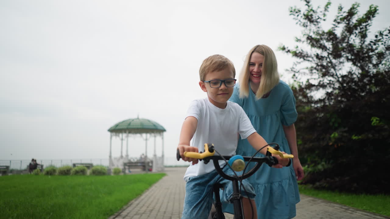 자전거를 타는 아들을 뒤에서 붙잡고 균형을 유지하도록 돕는 어머니의 가 따뜻한 순간