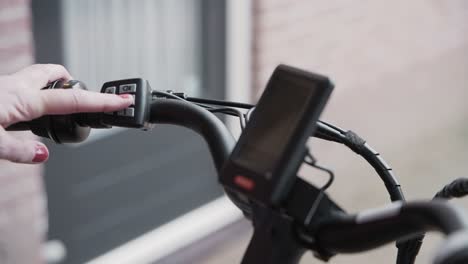 woman turns on the power to her e-bike with the controls on the handle bar and the display screen lights up