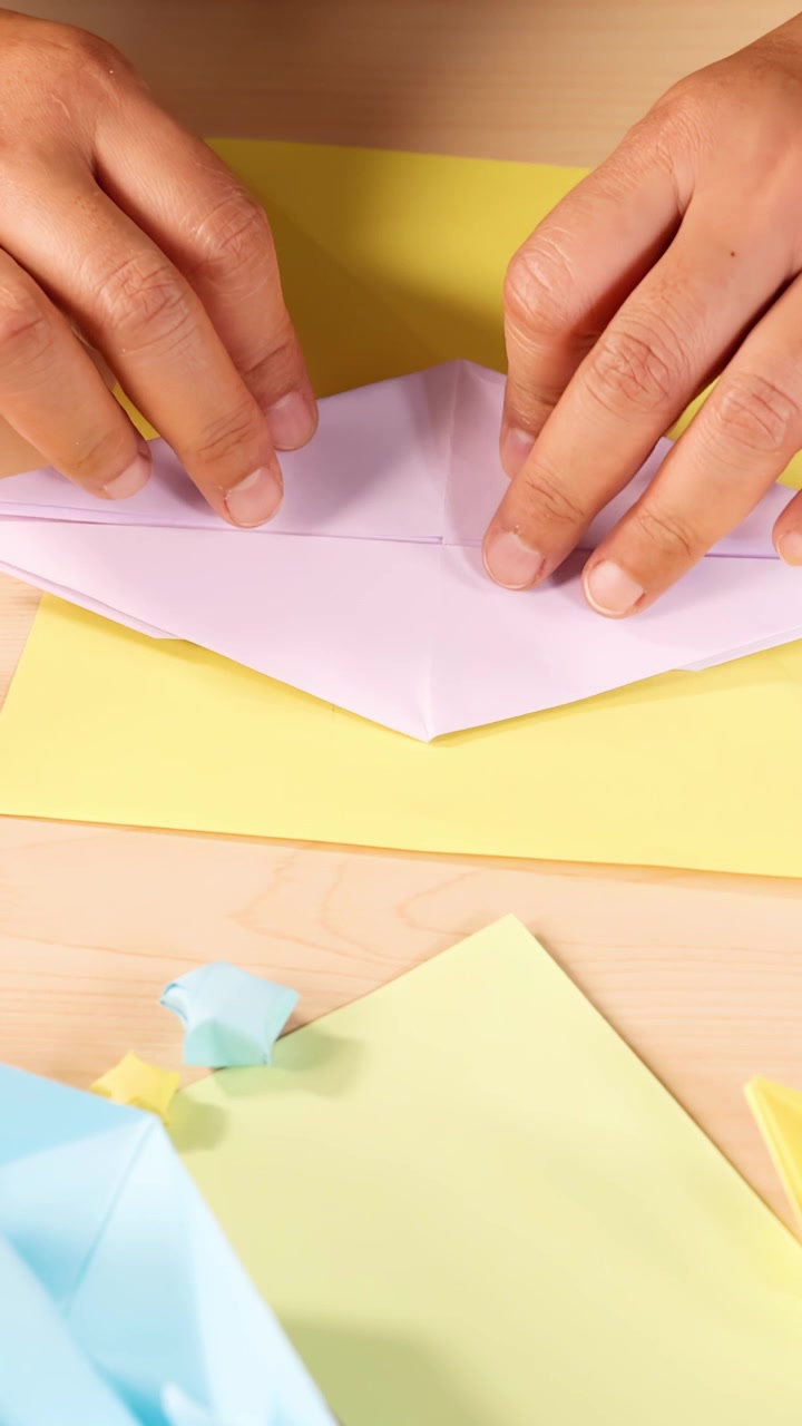 Una persona piega con cura carta origami pastello sulla scrivania, illuminazione brillante, prospettiva ravvicinata dall'alto