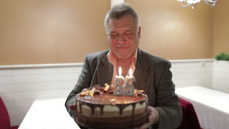 Happy-respectable-old-man-holding-cake.-Celebrating.-Blowing-birthday-candles