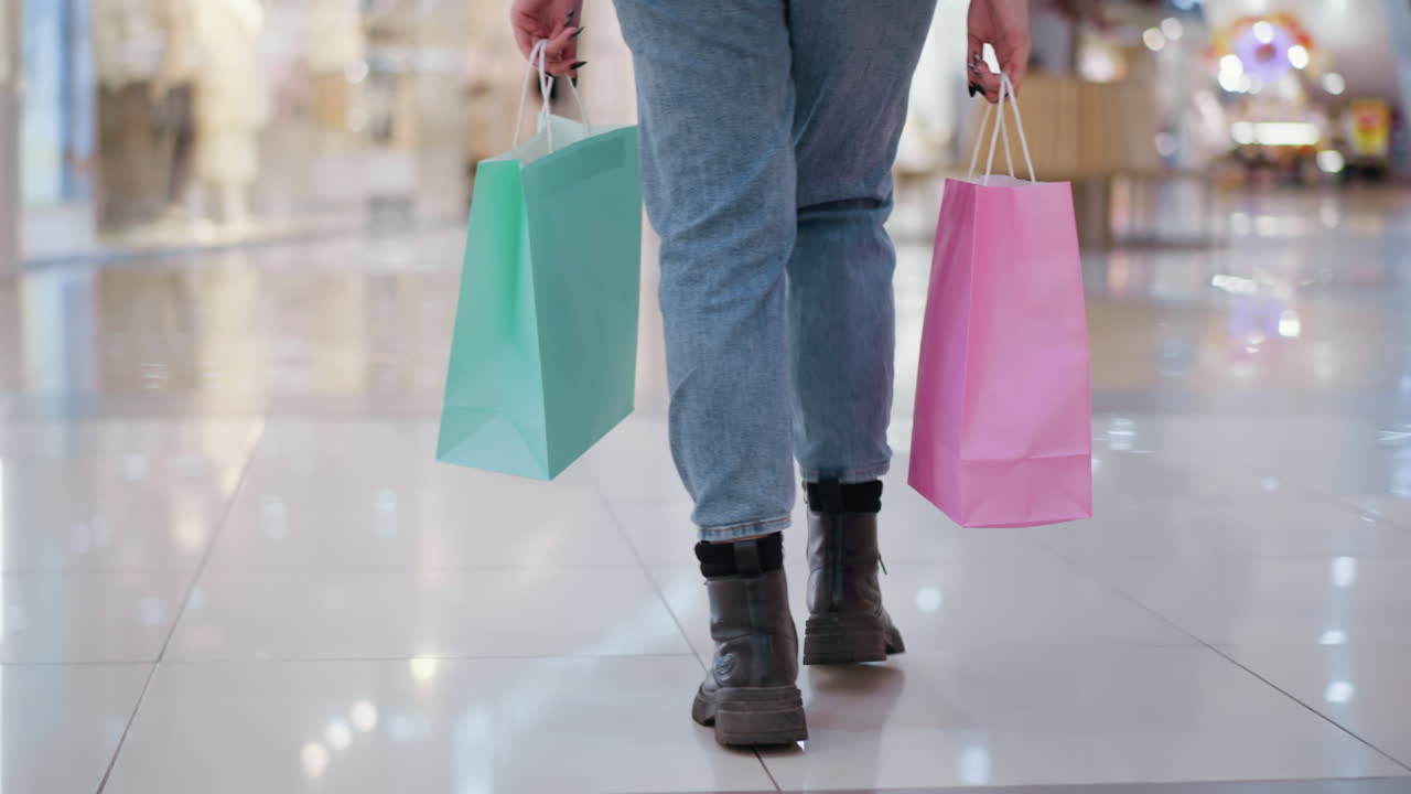 분홍색과 민트 쇼핑 가방을 가진 여자의 다리 시각 빛을 반영하는 반이는 쇼핑몰 타일에서 고, 다른 쇼핑객과 함께 흐릿한 배경