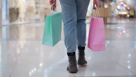 vista de la pierna de la dama con bolsas de compras rosas y menta caminando sobre azulejos brillantes del centro comercial que reflejan la luz, fondo borroso con otros compradores
