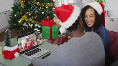 African-american-couple-wearing-santa-hats-having-a-videocall-on-laptop-at-home-during-christmas