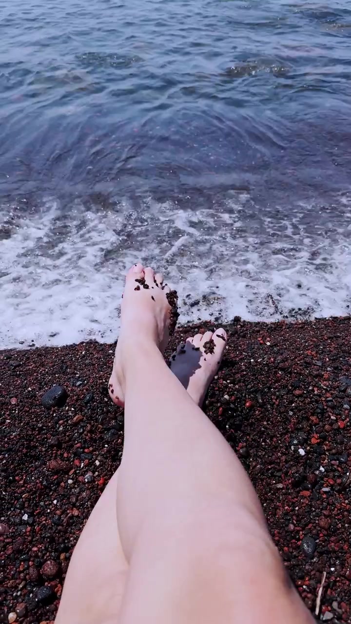 Gambe di donna che si rilassano sulla spiaggia rossa di Santorini in Grecia