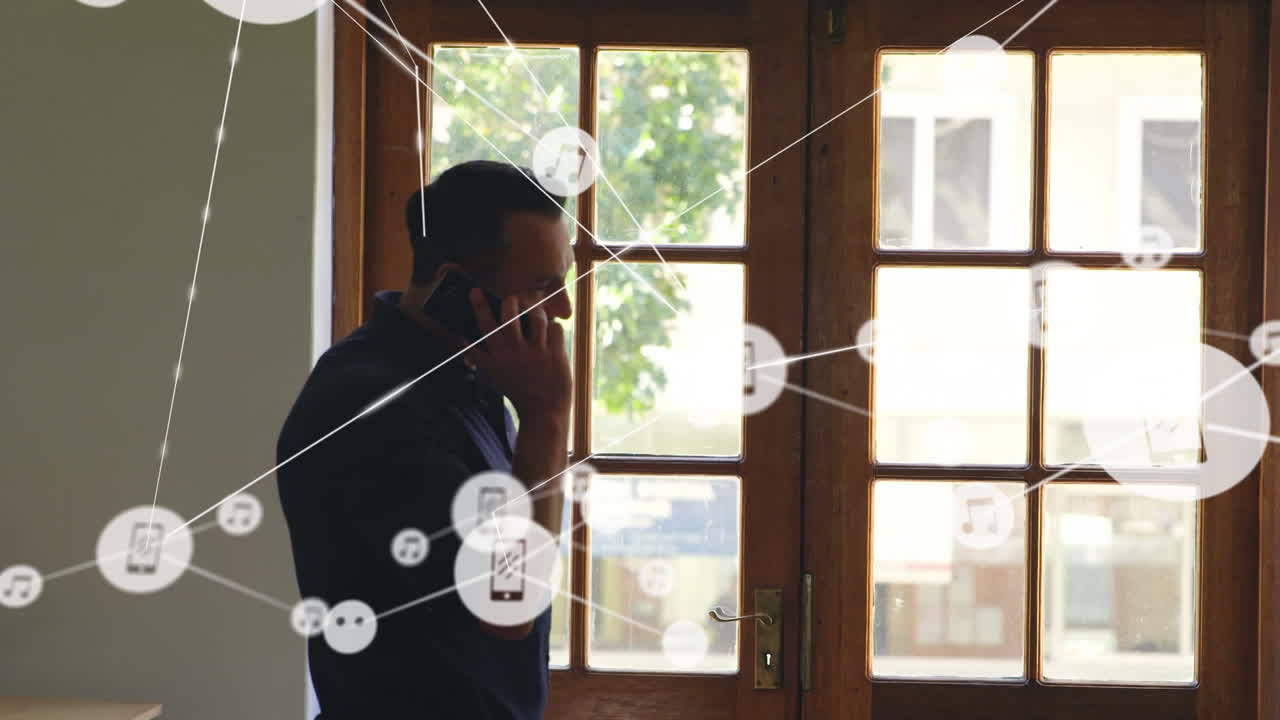 red de iconos digitales contra hombre caucásico hablando en teléfono inteligente cerca de la ventana en casa