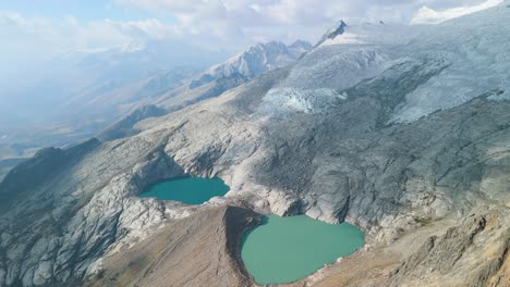 aerial pan revealing the dramatic rocky terrain, glacial slopes, and twin turquoise lakes of paso del zorro high in peru’s cordillera blanca mountains