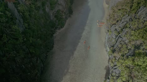 rising aerial of canoes in water by bushy cliffs in sunny philippines