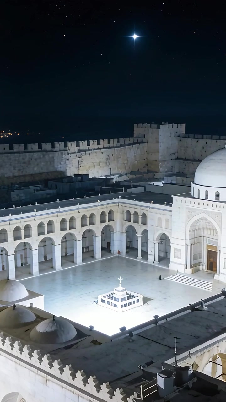 Video verticale: Inquadratura panoramica del cortile di una moschea di notte, con fontana illuminata e una persona in abito sotto un portico.
