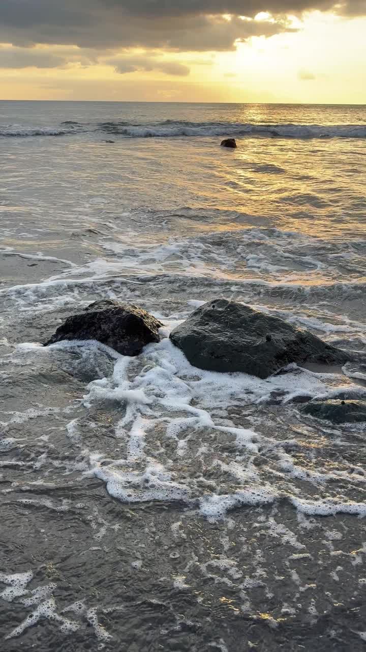 Onde dell'oceano che si infrangono sulle rocce al tramonto su una spiaggia sabbiosa.