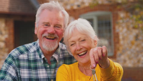 retrato de una feliz pareja de ancianos jubilados fuera de la cabaña sosteniendo la llave de la casa de ensueño