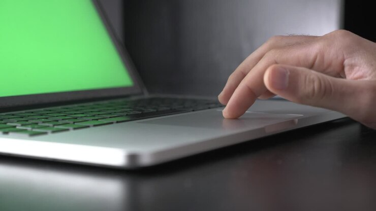 Man is using touchpad on laptop computer with green screen. Person is working on notebook with green screen in office. Businessman is using chroma key screen laptop computer on desk at home