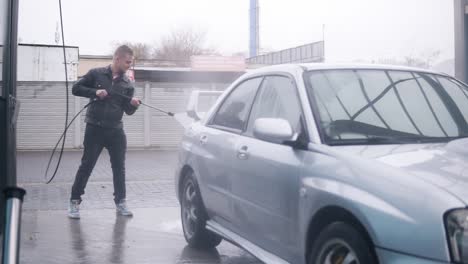 young attractive stylish man carefully washing his silver sportcar with water jet on self-service carwash. slowmotion shot