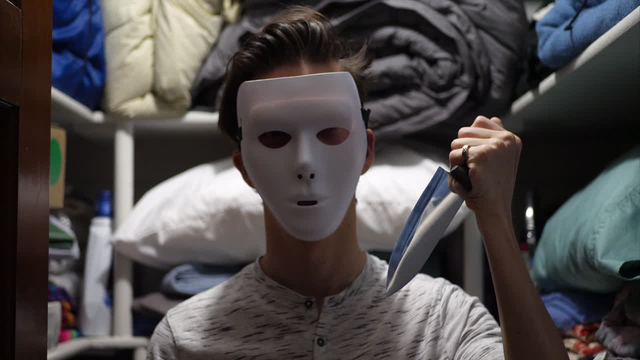 A scary slasher killer in a halloween mask with a knife hiding to attack his murder victim with creepy flickering lights