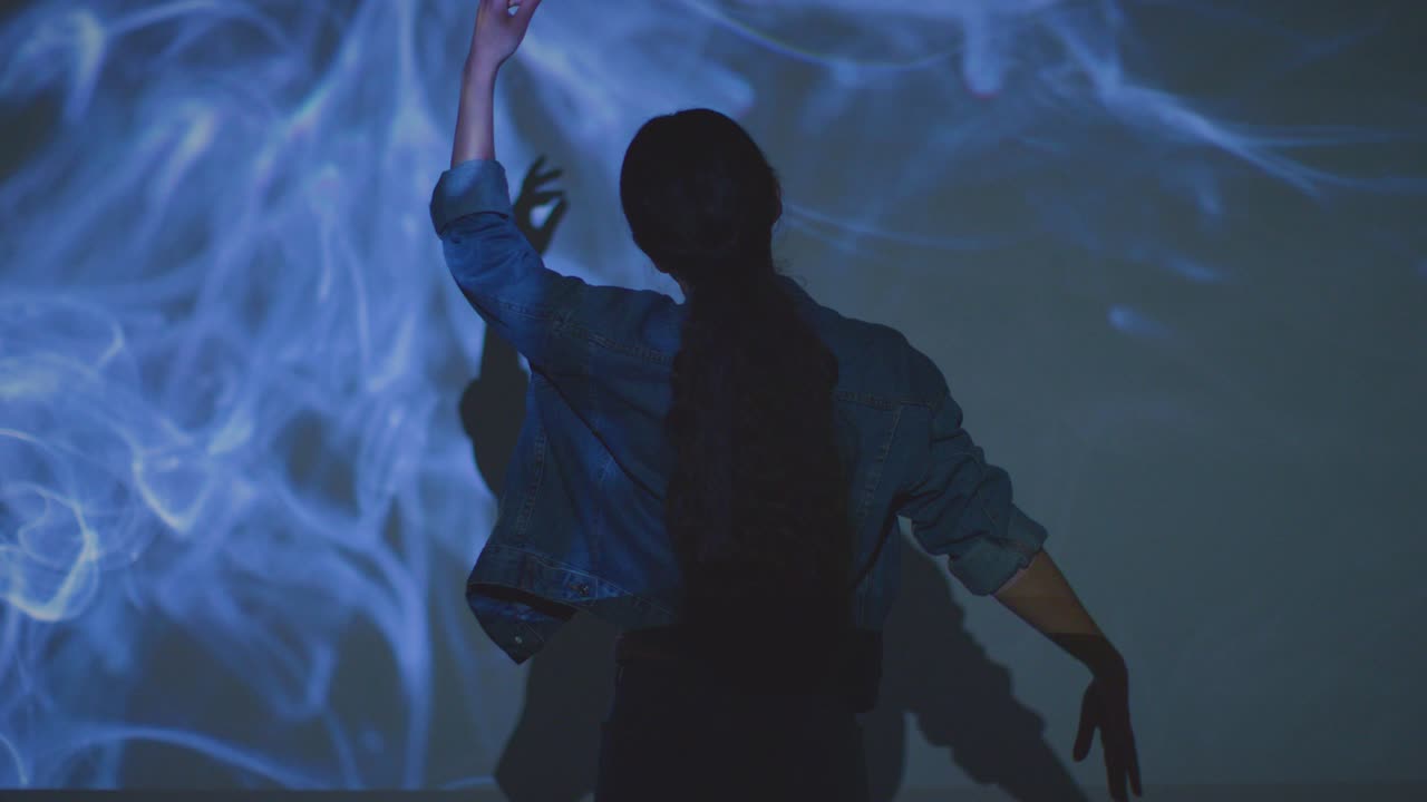 женщина посещает выставку иммерсивного искусства, взаимодействуя с изображениями дыма, проецируемыми на стену 1