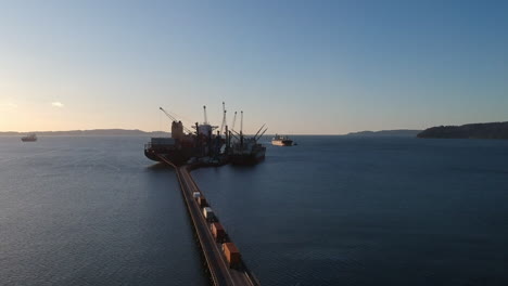 Los-Camiones-Se-Mueven-Por-El-Puente-Hacia-El-Puerto-De-Envío-Industrial,-Vista-Aérea