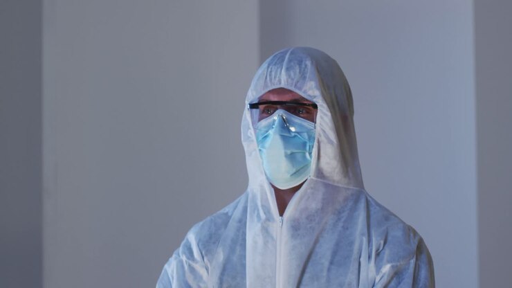 Ritratto di operatore sanitario uomo caucasico con indumenti protettivi, mascherina e occhiali protettivi