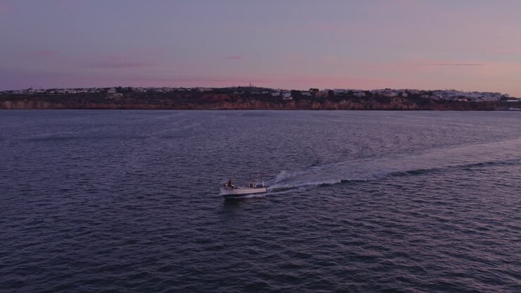 Orbita aerea intorno a un motoscafo che naviga nell'Oceano Atlantico vicino a Praia dos Arrifes all'alba.