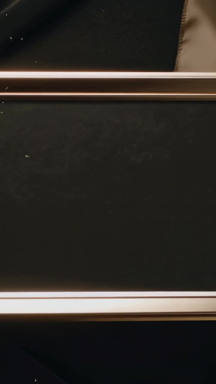 Vertical video: Tilting bronze frame shedding glitter onto dark drape, gold sash, showing finish