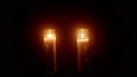 two candles flickering in front of a black background void