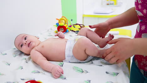 baby boy is at surgeon's check-up. female doctor examining baby's legs and knees. toys at the backdrop.