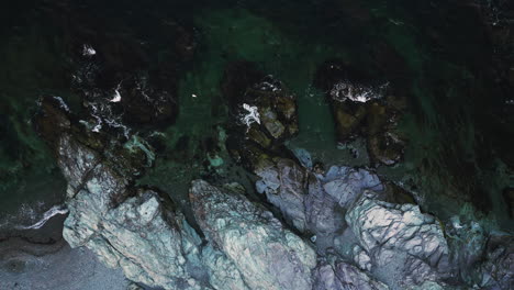 Aerial-top-down-static-of-white-rocky-coastline-with-seagulls-soaring-in-air