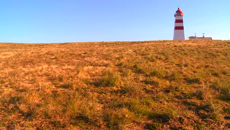 Ein-Hübscher-Rot-weißer-Leuchtturm-Steht-Auf-Einem-Grasbewachsenen-Hügel-In-Norwegen