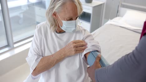 African-american-male-doctor-checking-blood-pressure-of-caucasian-female-patient-at-hospital