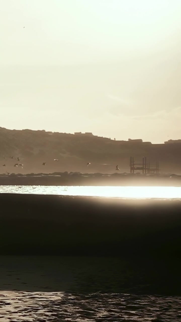 Video verticale: Corridore in tenuta sportiva che fa jogging all'alba, si muove lungo la sabbia bagnata oltre il mare illuminato dal sole, con spazio per il testo.