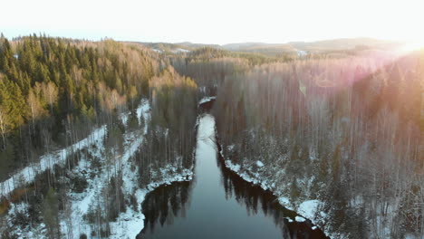 aerial, drone shot, above a river, sun flares, hitting leafless trees and first snow on the ground, on a sunny winter day, near joensuu, north karelia, finland
