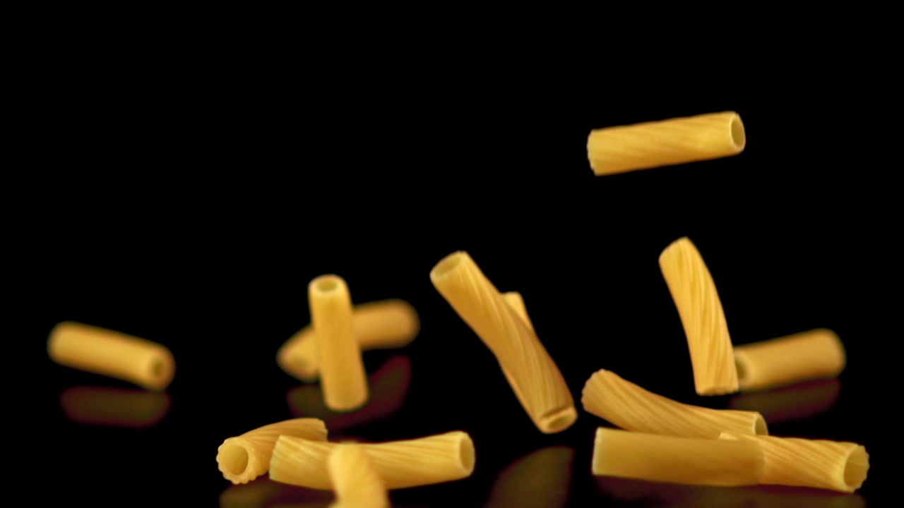 Pasta maccheroni secca che cade al rallentatore su sfondo nero.