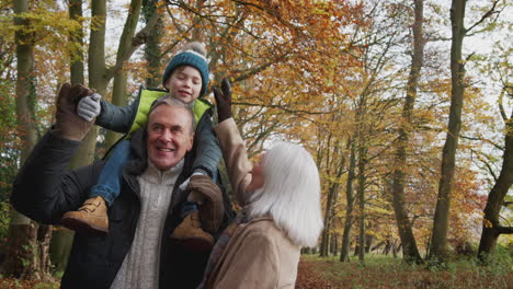 grandparents walking with grandson on grandfathers shoulders along path in autumn countryside