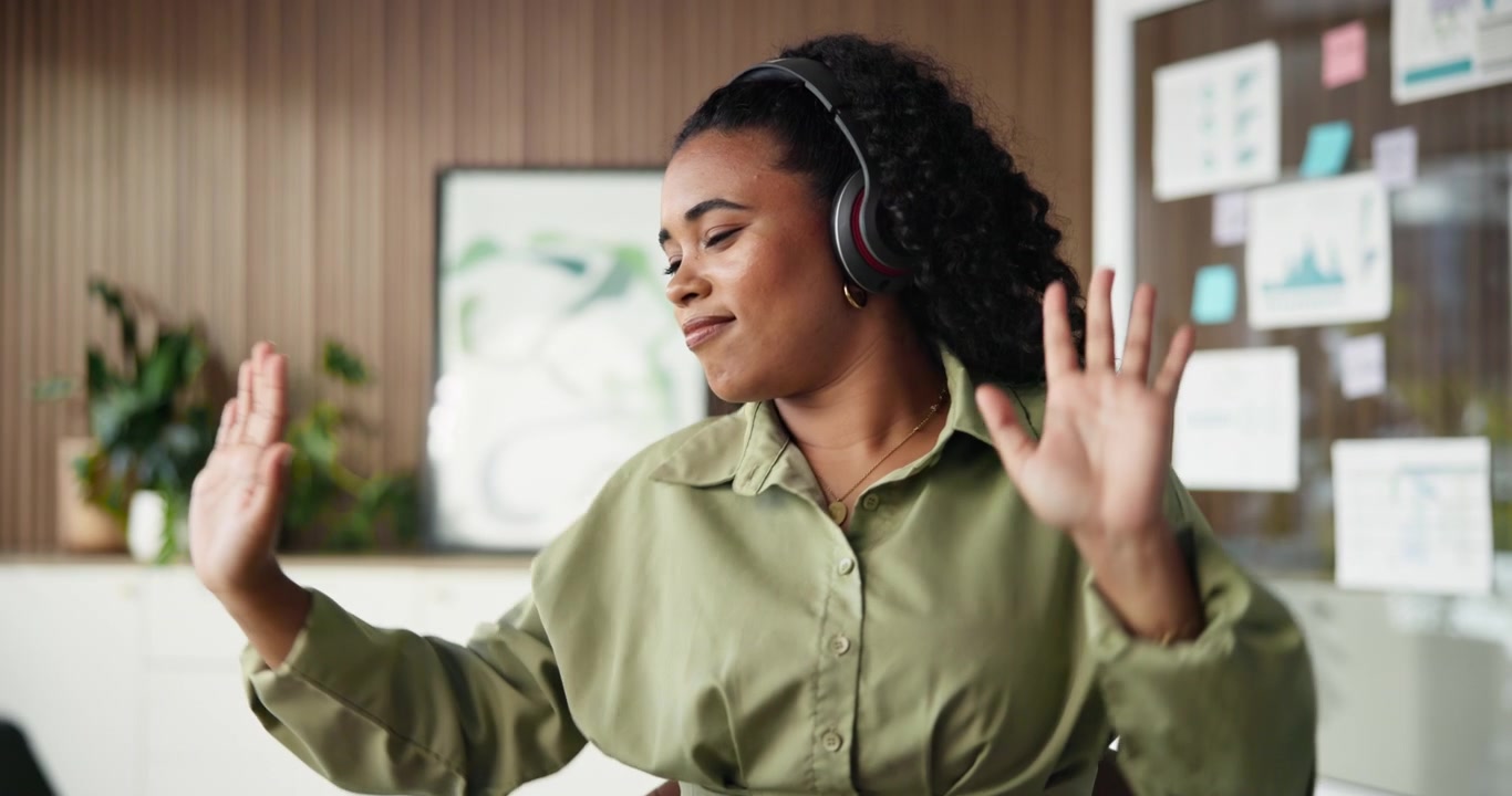 Ung kvinde med hovedtelefoner der danser ved sit skrivebord på kontoret