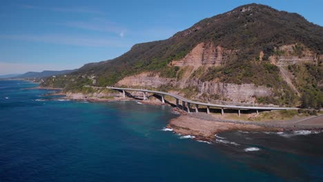 Aerial-view-of-Sea-Cliff-Bridge,-sunny-day,-grand-pacific-drive,-New-South-Wales,-Australia---backward-drone-shot