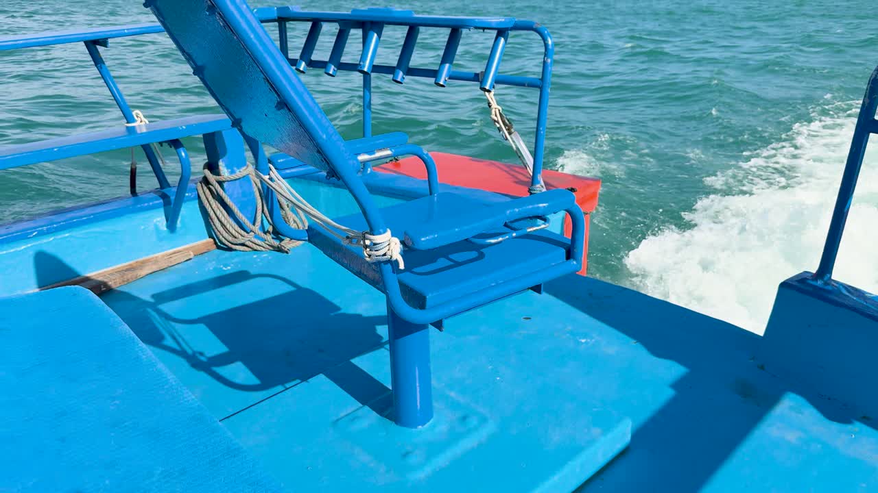 A vibrant blue fishing chair on a boat, cruising through Chalong Bay's turquoise waters under clear skies