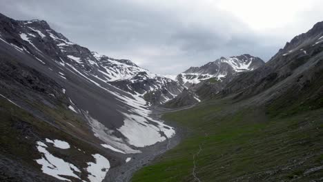 Aerial-drone-footage-flying-slowly-backwards-through-a-dramatic,-jagged-mountain-landscape,-looking-towards-a-grey-rocky-ridge-with-residual-patches-of-snow