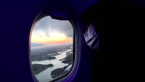 close up view of ethnic woman with a mask inside the plane and looking outside the window - handheld shot